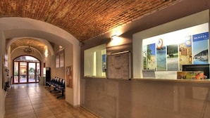 A hallway with a brick ceiling, a reception desk with hostel posters, and a seating area with chairs. - Hostel Marina (Cagliari)
