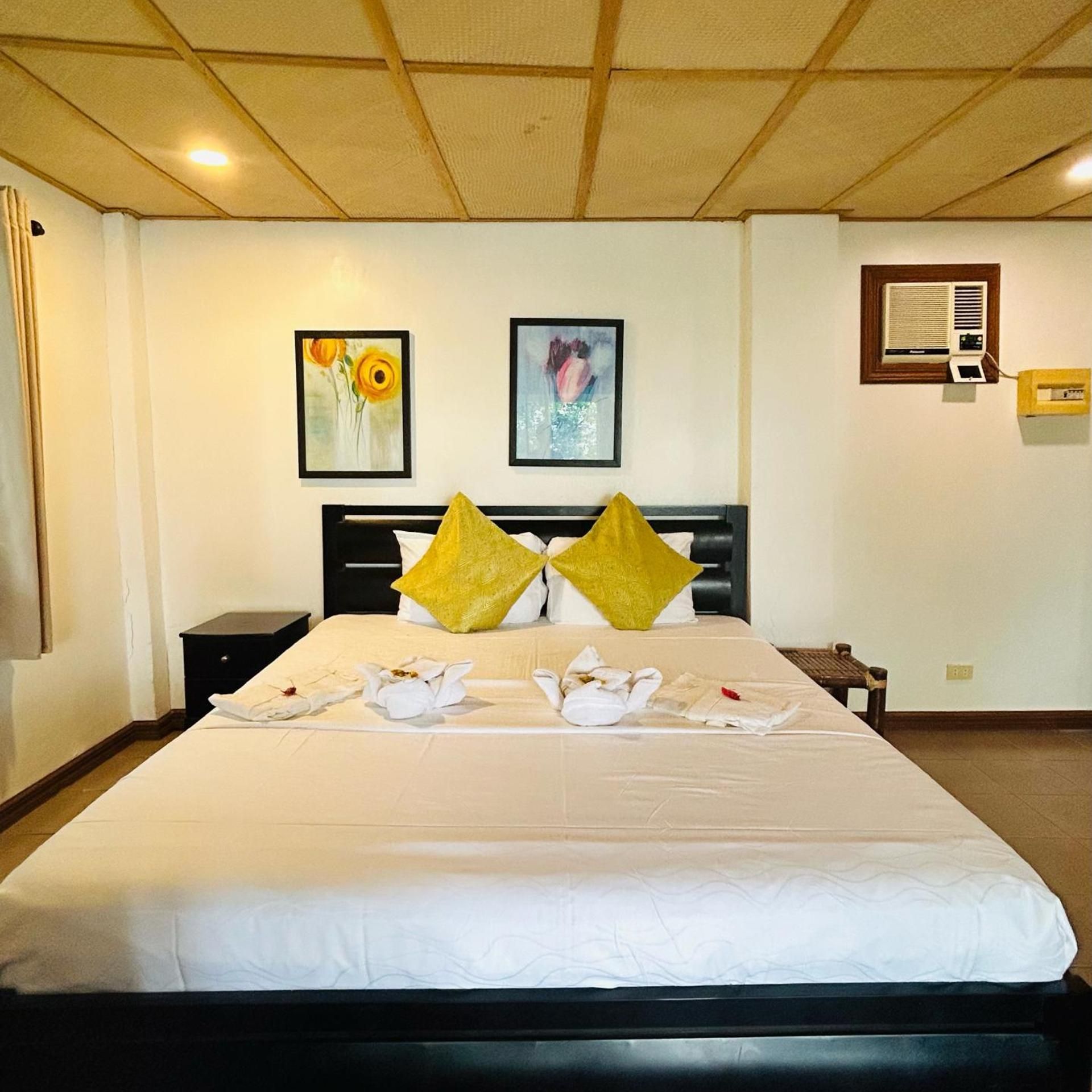 Een hotelkamer met een bed, twee schilderijen aan de muur, een verwarming en een klein tafeltje.