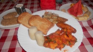 Une assiette de nourriture comprenant du pain, des saucisses et un plat à base de tomates, le tout servi sur une nappe à carreaux.