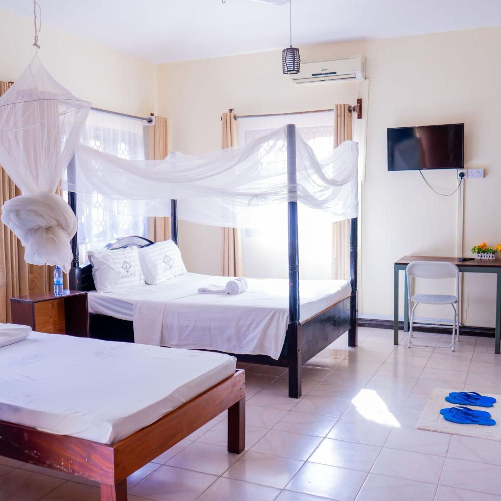 A hotel room with a four-poster bed, a desk, a chair, and a television.