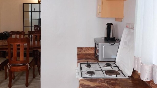 Een kleine keuken met een gasfornuis, een koffiezetapparaat en een klok aan de muur.