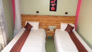 Een hotelkamer met twee bedden, elk voorzien van witte beddengoed en bruine hoofdeinden. Er is een houten hoofdeinde, een klein nachtkastje met een telefoon, en een wanddecoratie boven de bedden.