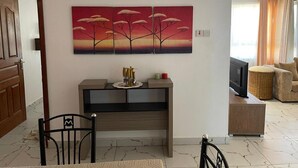 Een woonkamer met een televisie, een bank, een eethoek met stoelen en een schilderij aan de muur.