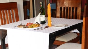 Een eettafel met een witte tafelkleed, een fles wijn, een lange kaars en borden met eten.