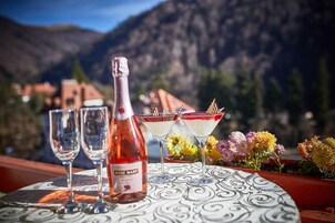 Una mesa con una botella de vino Rosado Mary, dos copas de vino y dos copas de martini con líquido rojo y adornos de chocolate, con montañas al fondo.