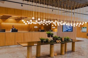 Un área de recepción moderna con un mostrador de madera, lámparas colgantes esféricas y una mesa con plantas y objetos decorativos.