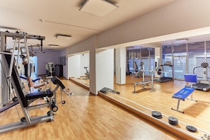 Ett gym med träningsutrustning, speglar och en blå bänk.