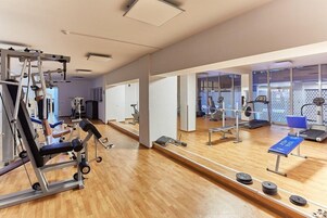 Un gimnasio con equipo de ejercicio, espejos y un banco azul.