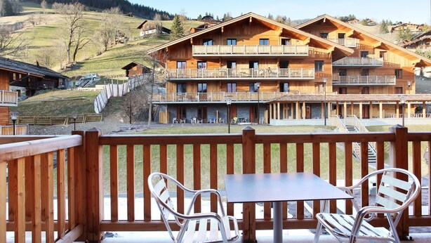 Ein Chalet-ähnliches Gebäude aus Holz mit mehreren Balkonen, Sitzgelegenheiten im Freien und Blick auf eine hügelige Landschaft.