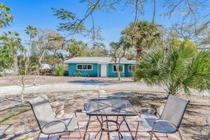 A house with a blue exterior, surrounded by palm trees and a patio with metal chairs and a table. - Tree House on 20th | Quick Walk to the Beach (Indian Rocks Beach)