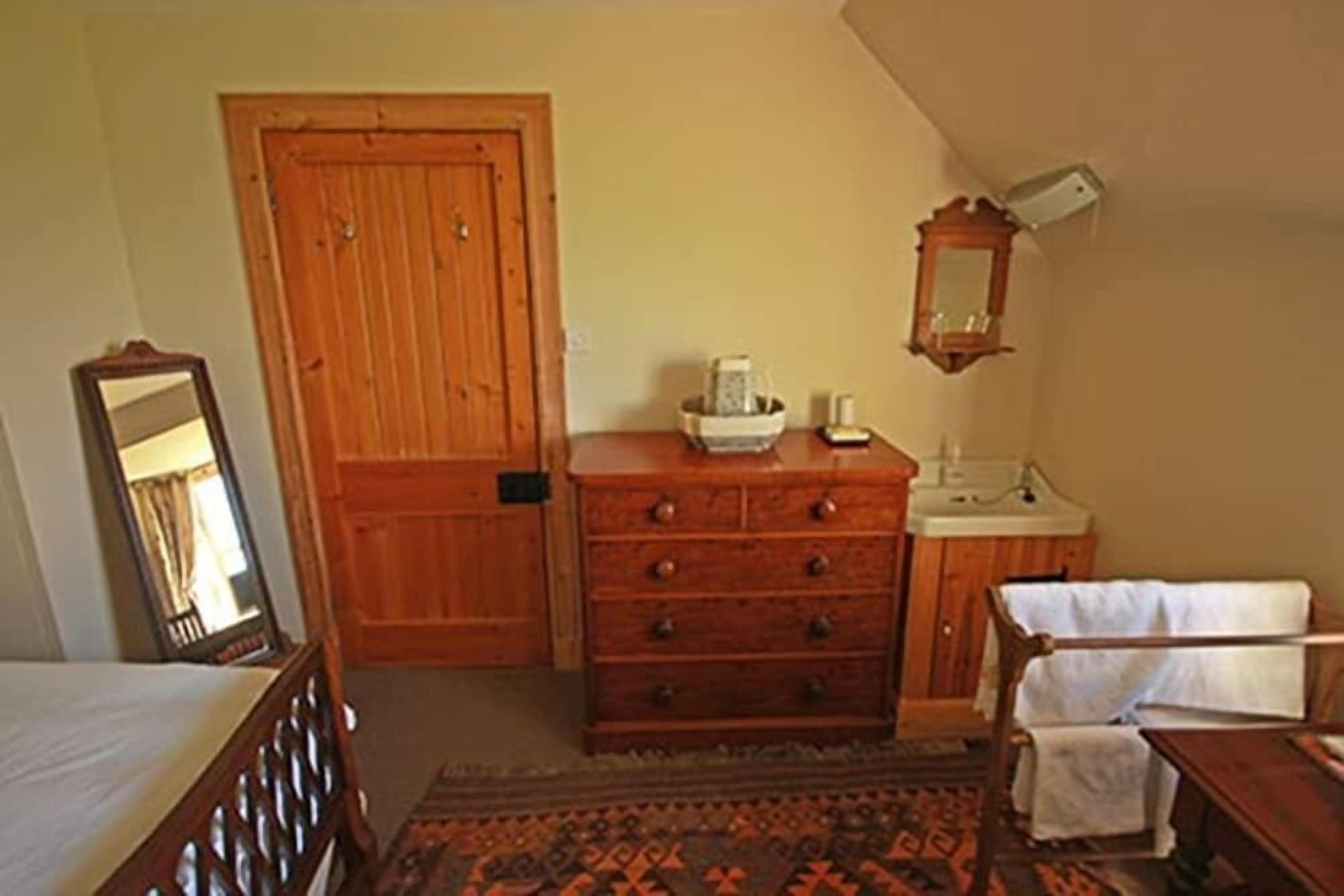 Ein Zimmer mit Holztür, einem Schrank mit Schubladen, einem Spiegel, einem Waschbecken und einem gemusterten Teppich.