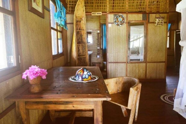 A wooden dining table with a vase of flowers and a decorative plate. A wooden chair is positioned at the table. - Pemba Lodge (Pemba Island)