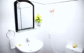A bathroom with a white sink, a glass shelf with a mirror, a towel ring, a small vase with yellow flowers, and a toilet with a tissue box. - Silver Dome (Ella)