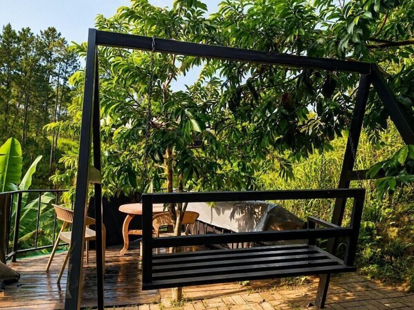 A wooden deck with a swing, surrounded by lush greenery. - Silver Dome (Ella)