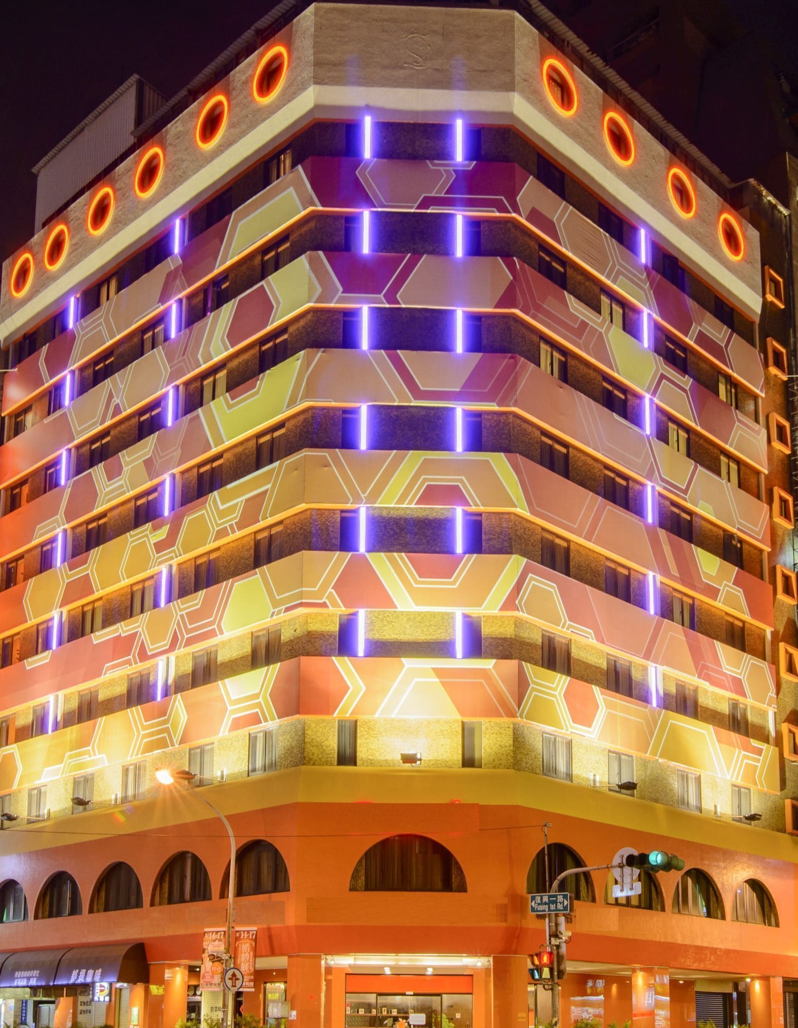 Un edificio de varios pisos con una fachada geométrica distintiva y luces de neón iluminadas.