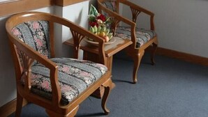 A corner of a room with two wooden chairs with floral upholstery and a small table with a vase of flowers.