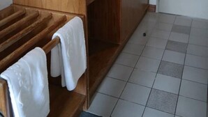 A wooden wardrobe with a white refrigerator inside, a bench with towels, and a tiled floor.