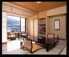 A traditional Japanese-style room with tatami flooring, a low table with chairs, a television, and a view of a mountainous landscape.