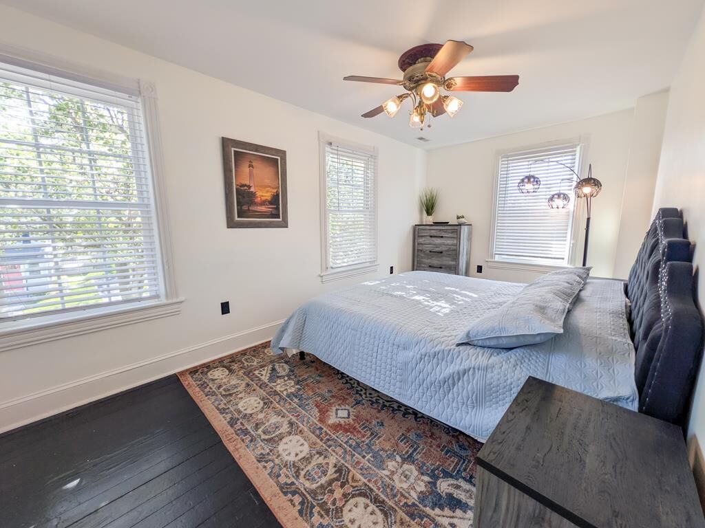 A bedroom with a bed, a ceiling fan, a nightstand, a lamp, and a window with blinds.