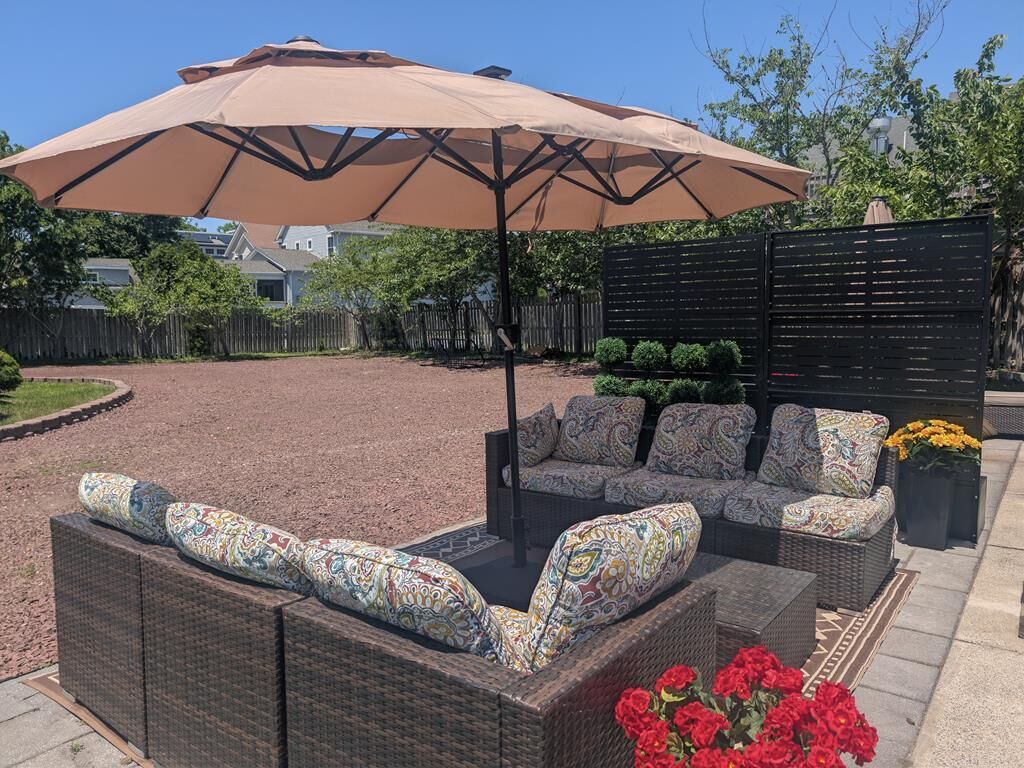 An outdoor patio with wicker furniture, a large umbrella, and a black fence.