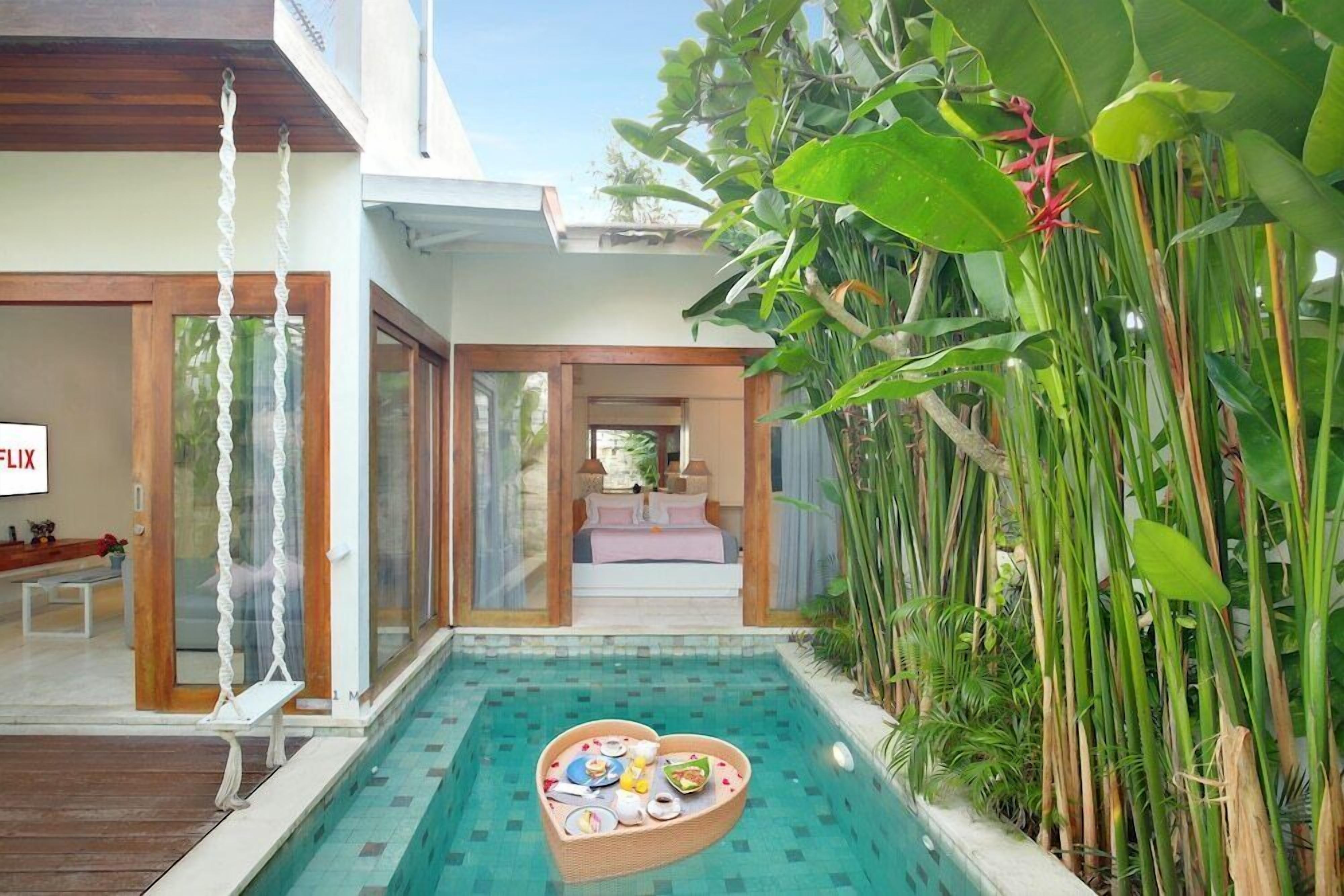 A modern house with a swimming pool, a dining area with a heart-shaped table, and lush greenery.