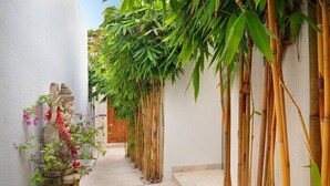 A narrow pathway flanked by bamboo plants and a statue. - The Jimbaran Beach Villa by Ini Vie Hospitality (Jimbaran)