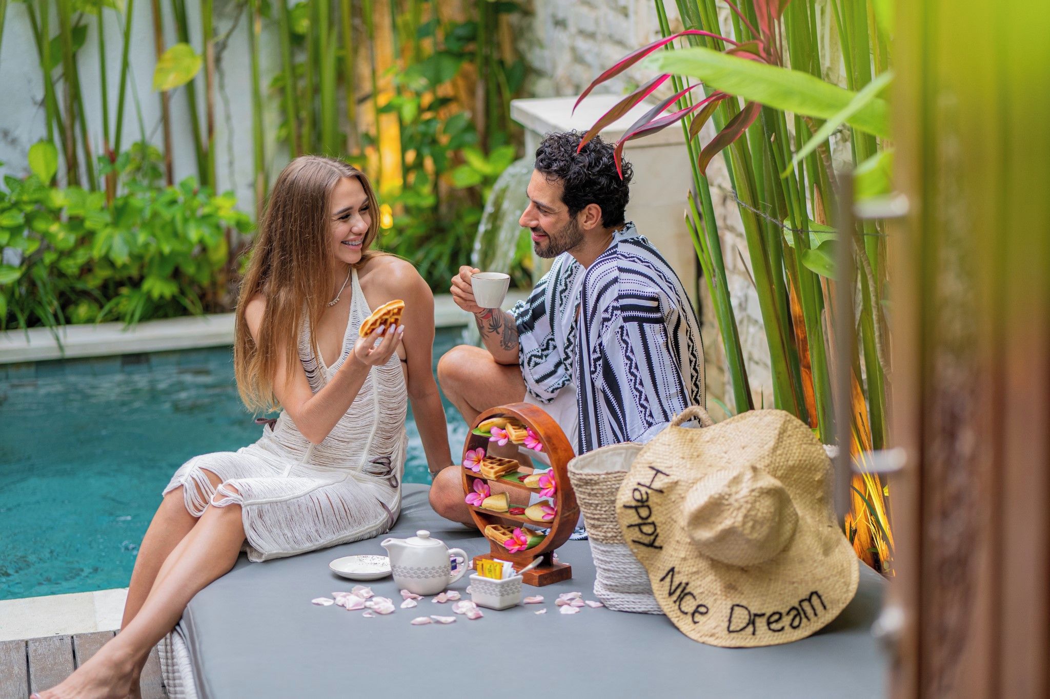 Two people sitting by a pool with a waffle display and a hat labeled 'Happy Nice Dream'.