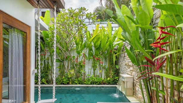 A pool area with a wooden deck, a swing, and lush tropical plants. - The Jimbaran Beach Villa by Ini Vie Hospitality (Jimbaran)