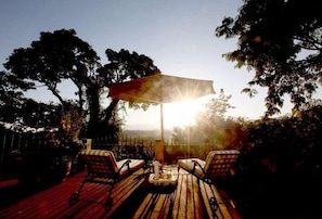 Eine Terrass mit zwei Liegestühlen und einem Tisch, umgeben von Bäumen und Blick auf die Landschaft.