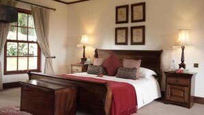 A bedroom with a large bed, wooden headboard, two bedside tables with lamps, a nightstand, and a window with curtains. - The Manor Ngorongoro (Karatu)