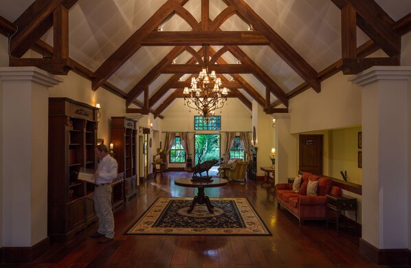 A spacious lobby with high ceilings, exposed wooden beams, a chandelier, a large rug, a sofa, and a fireplace.
