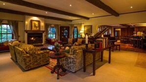 A spacious living room with a fireplace, a grand piano, and a dining area with a bar. - The Manor Ngorongoro (Karatu)