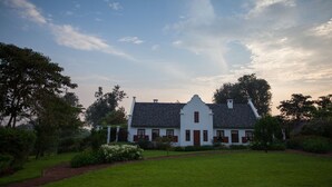 A white building with a steeply pitched roof, surrounded by a well-maintained lawn and trees. - The Manor Ngorongoro (Karatu)