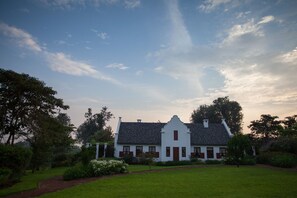 A white building with a steeply pitched roof, surrounded by a well-maintained lawn and trees.