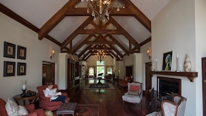 A spacious living room with high ceilings, wooden beams, a fireplace, and a chandelier. - The Manor Ngorongoro (Karatu)