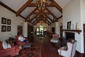 A spacious living room with high ceilings, wooden beams, a fireplace, and a chandelier.