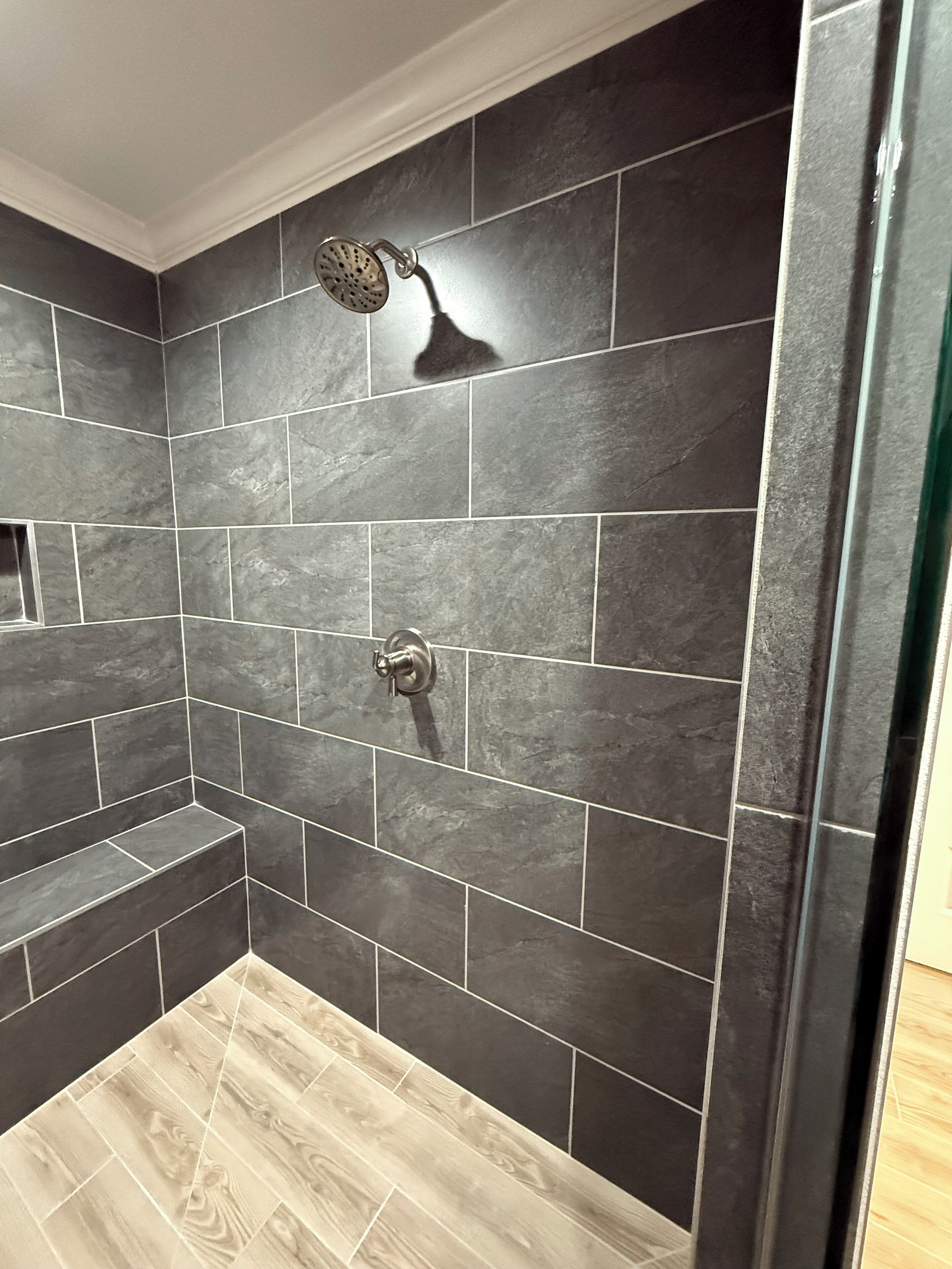 Un área de ducha con azulejos oscuros y suelo de madera.