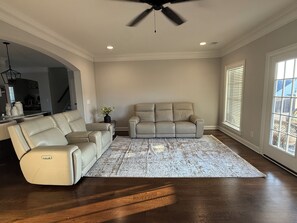 A spacious living room with a beige sectional sofa, a small side table with a vase, and a patterned rug. - Spacious 4Bd/4bath Home with Media Room-Great for Master’s Week! (Evans)