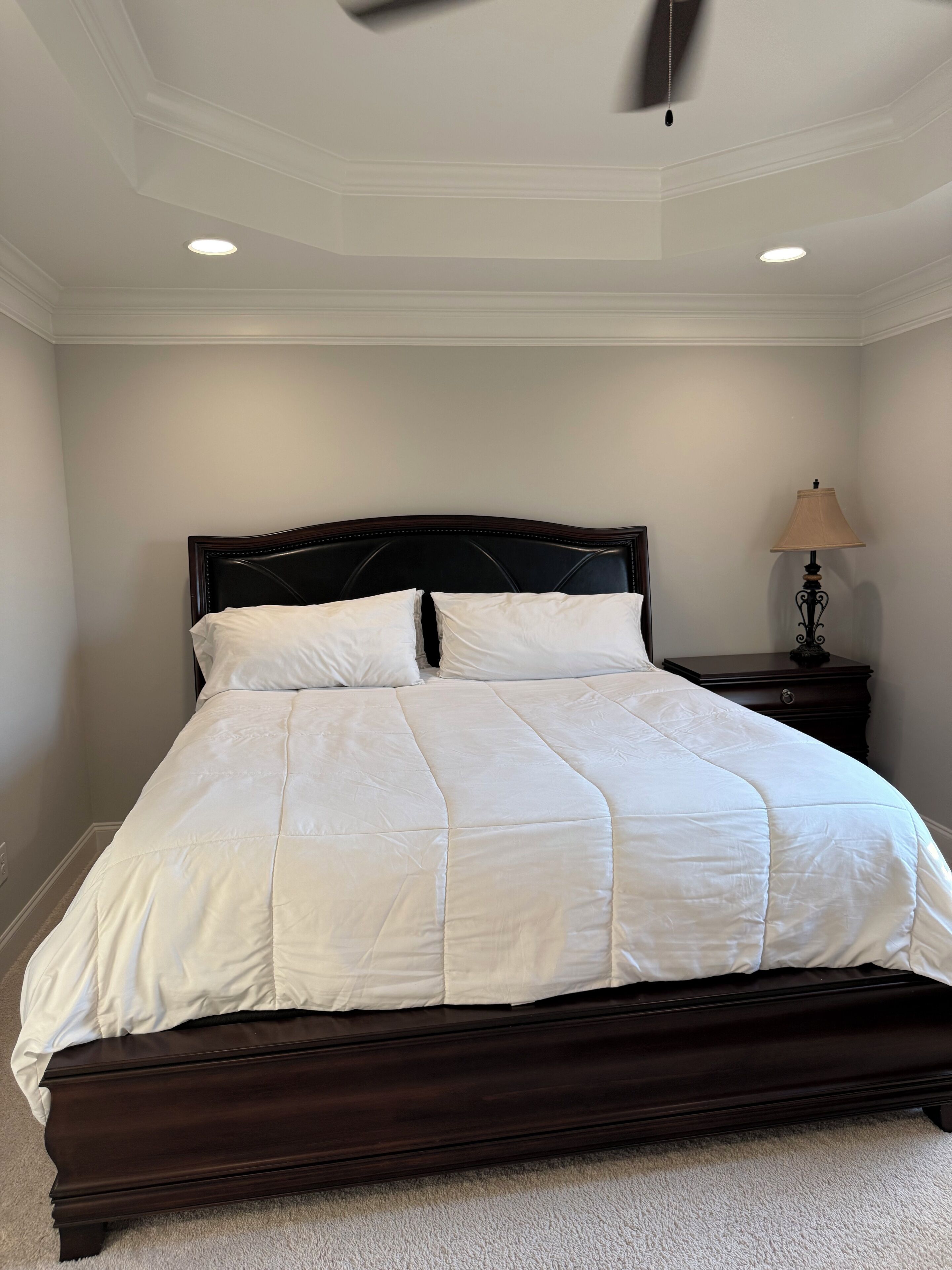 A neatly made bed with a dark headboard in a room with white walls and a ceiling fan.
