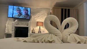 A hotel room with a large bed, a television displaying a movie, a fireplace, and a decorative swan towel arrangement. - Harrys Steakhouse & Beach Hotel (Patong)