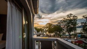 A balcony with a view of a sunset over a beach, a sofa, and a railing. - Harrys Steakhouse & Beach Hotel (Patong)