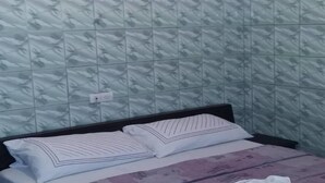 A bedroom with a patterned wall, a bed with two pillows, and a power outlet on the wall. - Hotel La Citadelle (Abidjan)