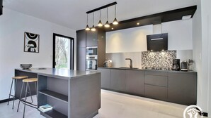 Een moderne keuken met een centraal eiland, barkrukken, een groot raam en een betegelde spatwand.