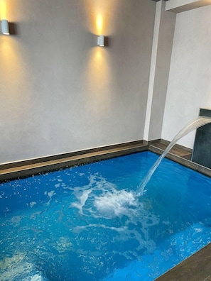 Une piscine dans laquelle l’eau s’écoule, entourée d’un mur sobre agrémenté de deux lampes fixées au mur.