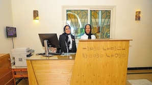 A reception desk with two individuals standing behind it, a computer monitor, and a printer to the left.
