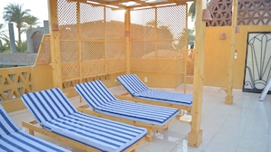 A sunlit outdoor lounge area with wooden loungers and a pergola structure.