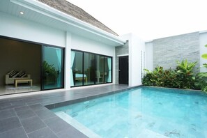 A modern house with a swimming pool, large sliding glass doors, and a stone wall. - Layantara Resort (Thep Krasattri)