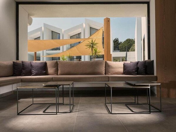 Een moderne woonkamer met een grote hoekbank, twee glazen salontafels en uitzicht op een modern gebouw met een geel dak.