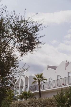 A modern building with a white facade, multiple balconies, and a palm tree in the foreground. - Cavo Vezal (Zakynthos)