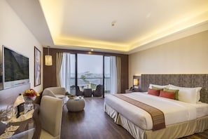Une chambre d’hôtel moderne dotée d’un grand lit, d’un coin salon avec une table en verre et offrant une vue sur l’extérieur grâce à de grandes fenêtres.